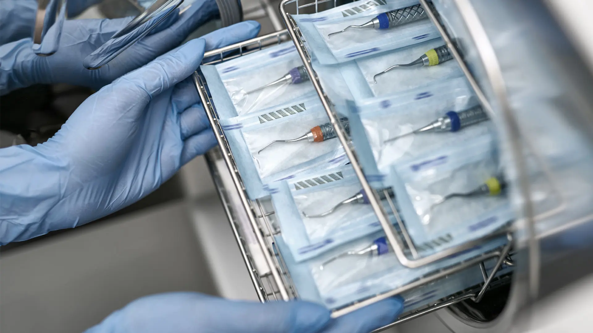 Gloved clinician loading wrapped dental instruments into an autoclave tray
