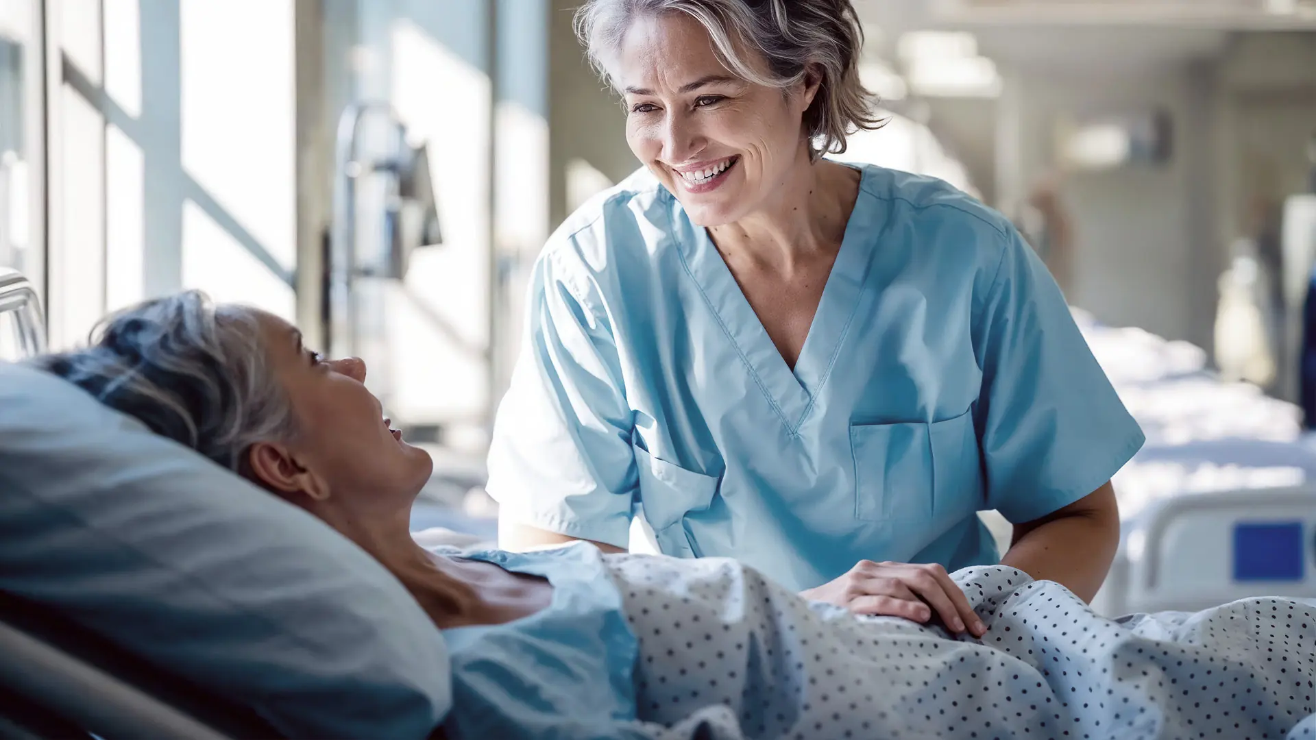 Clinician in blue scrubs speaking with a patient in a hospital room